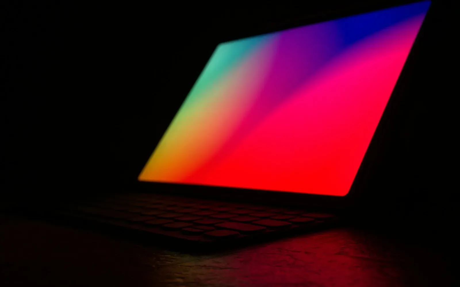 Laptop mit farbig leuchtendem Bildschirm in völliger Dunkelheit