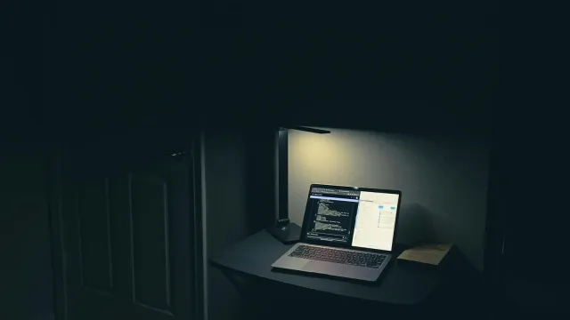 Aufgeklappter Laptop auf einem Tisch in einem dunklen Raum – Webcam Privatsphäre beim Camsex
