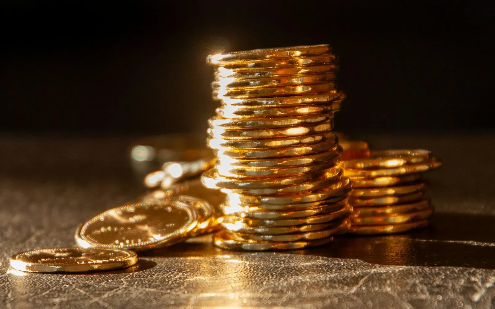 Stapel goldener Münzen auf einer dunklen, glänzenden Oberfläche