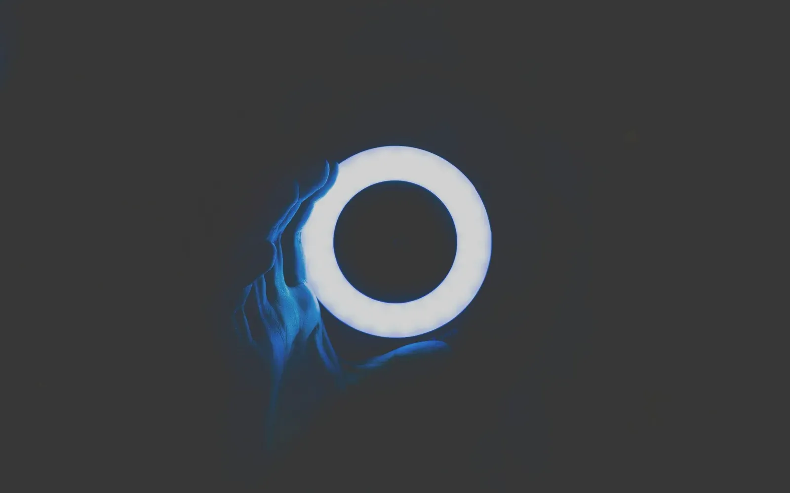 Ein leuchtendes Ringlicht vor dunklem Hintergrund, davor eine Hand im blauen Licht – Camgirl werden