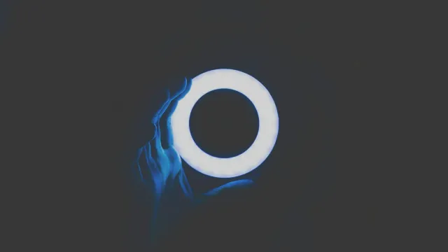 Ein leuchtendes Ringlicht vor dunklem Hintergrund, davor eine Hand im blauen Licht – Camgirl werden